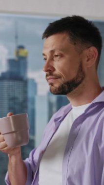 Şık bir adam, çağdaş ve modern bir mekanda, çarpıcı bir şehir manzarası olan bir fincan kahve tutuyor.