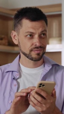 Bir adam akıllı telefonuna dikkatle bakıyor, derin düşüncelere dalmış, çağdaş bir ev ortamının ortasında.