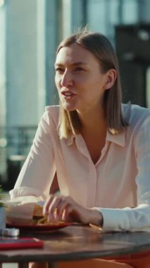 Bir kadın dışarıda bir kafe masasında oturuyor, gün boyunca mutlu bir şekilde atıştırıyor ve neşeli bir sohbete dalıyor.
