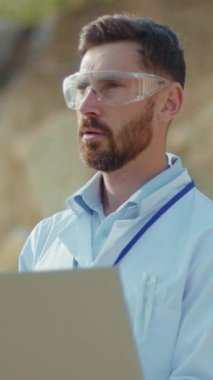 Güvenlik gözlüğü takan kendini adamış bir bilimadamı, açık hava ortamında bilgisayardaki verileri titizlikle inceliyor.