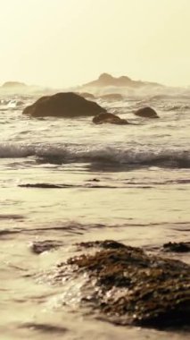 Huzurlu ve sakin bir manzara, yumuşak dalgaların güzel sisli bir sabah ışığında engebeli kayalara hafifçe çarpması.