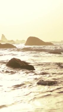 Huzurlu ve sakin bir deniz manzarası, parıldayan dalgalar ve sıcak altın ışıkla aydınlatılmış engebeli kayalar.