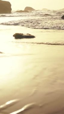 Bu gün batımında huzurlu ve huzurlu bir sahil sahnesi, hafif dalgalar geliyor ve uzaktaki kayalar.