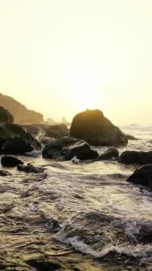 Güneşin güzel, sakin bir manzarası zarif bir şekilde kayalık kıyıların üzerinde batıyor. Yumuşak dalgalar kıyıları okşuyor.