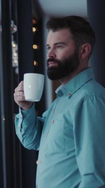 Sakallı bir adam sabah rutinini sakin ortamlarda bir fincan kahveyle sükuneti ve ayinin basit zevkini taşıyarak yapar.