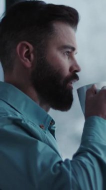 Bu video, sakallı bir adamı, sakin bir atmosferde, pencerenin kenarında, kahvesini yudumlarken ve dışarıyı seyrederken gösteriyor.