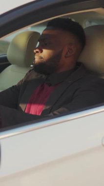 Bu videoda, takım elbiseli iyi giyimli bir adam şehir manzarasında beyaz bir araba sürüyor, sofistike ve modern yaşam tarzı sergiliyor.