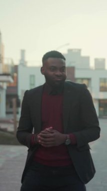 Takım elbiseli ve kırmızı kazaklı iyi giyimli bir adamı takip edin. Kentli bir çevrede rahatça dolaşır, stil ve profesyonellik gösterir.