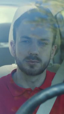 Bakımlı sakallı bir adam bir arabanın sürücü koltuğunda rahatça oturuyor ve önündeki yola bakıyor.