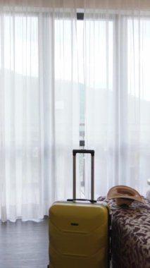 Zarif perdelerle birlikte güzelce paketlenmiş bir bavulu olan parlak ve misafirperdeli bir otel odası.