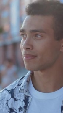 Genç bir adam hayat dolu canlı bir şehir zeminiyle çevriliyken düşünceli bir şekilde uzaklara bakar.