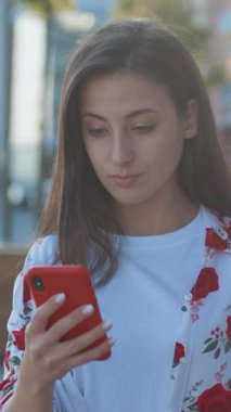 Genç bir kadın telefonuna derinden konsantre olmuş, kendini kentsel bir manzaranın ortasında ve canlı, çiçek açan bir doğanın ortasında buluyor.