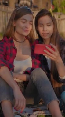 İki genç arkadaş açık havada akıllı bir telefona bakarken keyifli ve neşeli bir anın tadını çıkarıyorlar.