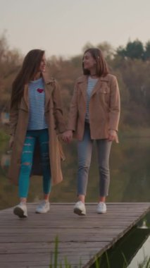 İki yakın arkadaş el ele tutuşurken onlar da göl kenarında huzurlu ve huzurlu bir sonbahar gezintisi yapıyorlar.