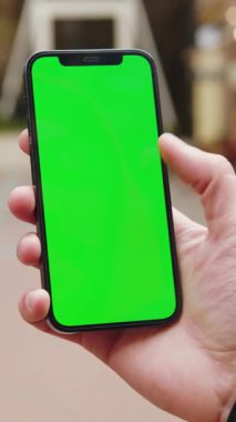 Bir birey bir uygulamayı düzenlemek veya görüntülemek için kullanılan yeşil ekranı gösteren bir akıllı telefon tutuyor