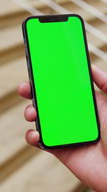 Bir kişi rahat bir şekilde canlı yeşil ekran içeren bir akıllı telefon tutar, dijital reklam veya uygulama modellemeleri için idealdir