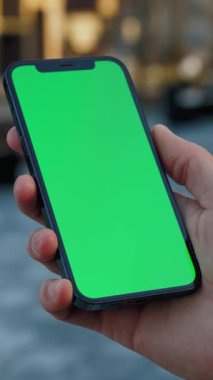 Bir akıllı telefon bekletiliyor, dijital medya veya reklam oluşturmak için ideal olan yeşil bir ekran sergiliyor