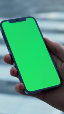 Bir el, çeşitli medya projeleri için ideal, canlı yeşil bir ekran gösteren parlak bir akıllı telefonu sıkıca tutar