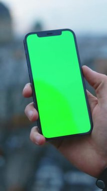 Bir birey, açık havada uygulamaları göstermek için mükemmel olan canlı yeşil ekran içeren bir akıllı telefon tutuyor.