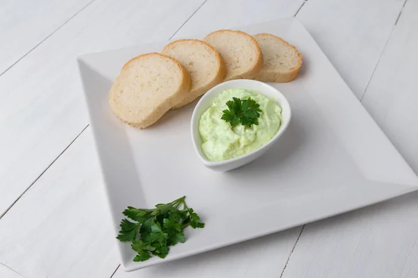 Beyaz kare tabakta avokado sosu ve ekmek dilimleri. Ahşap arka plan vejetaryen restoranı.