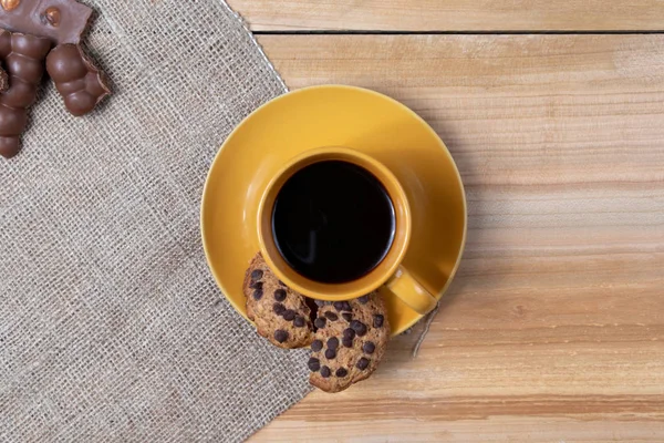 Bir fincan sade kahve, ev yapımı çikolatalı kurabiyeler ahşap arka planda günün başlangıcında aromatik aromalar.
