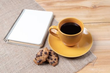 Bir fincan sade kahve, ev yapımı kurabiyeler, ahşap arka planda çikolata kırıntıları, defter planı, tatil günü iş görüşmesi.