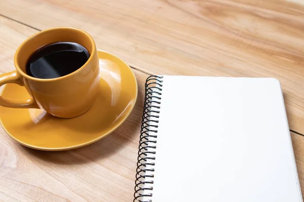 Bir fincan sade kahve ve ahşap arka planda defter planı. Tatil günü iş görüşmesi.