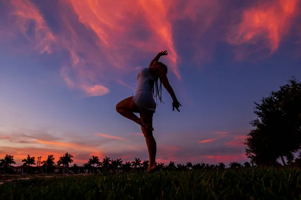 Woman silhouette dancing in the sunset with red clouds in the sky