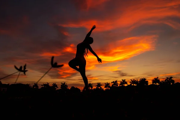 Woman silhouette dancing in the sunset with red clouds in the sky