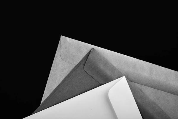 Photo of blank envelopes on a black background. Template for branding identity. Envelopes mockup. White paper isolated on black. Top view.