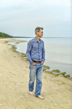 Denizin kenarında yürüyen bir adam.