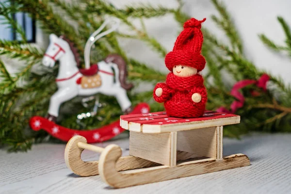 圣诞卡 在圣诞树和玩具马的背景下 圣诞老人雪橇上穿着针织衣服的明亮的红色玩具孩子 — 图库照片