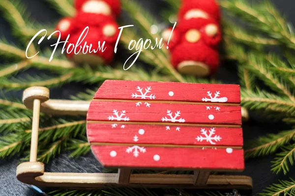 圣诞卡 明亮的红色圣诞老人的雪橇与雪花在圣诞树的背景和一个木制的婴儿在明亮的红色针织衣服 俄罗斯的题词新年快乐 — 图库照片