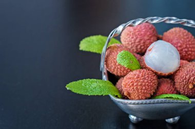 Taze organik liçi meyvesi metal kasede bacakları siyah arka planda, üst manzara