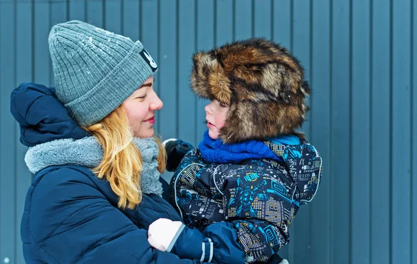 Junge Glückliche Frau Mit Sohn Arm Auf Blaugrauem Zaunhintergrund Winter — Stockfoto