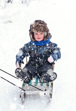 Kar kızağında kürk şapkalı güzel çocuk.