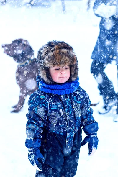 雪の中で屋外で遊んで毛皮の帽子の服の面白い男の子 寒い雪の日には冬の子供たちと積極的な休息 血を流す子供 — ストック写真