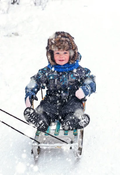 Kar kızağında kürk şapkalı güzel çocuk.