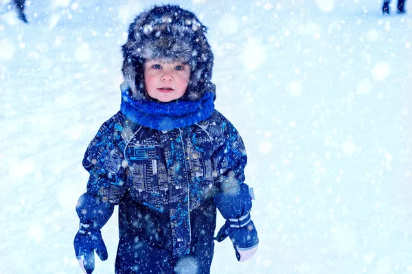 雪の中で屋外で遊んで全体と毛皮の帽子の服で面白い小さな男の子 寒い雪の日には冬の子供たちと積極的な休息 幸せな子供 — ストック写真