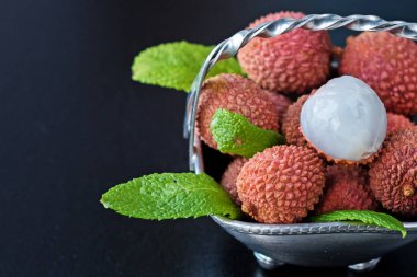 Taze organik liçi meyvesi metal kasede bacakları siyah arka planda, üst manzara