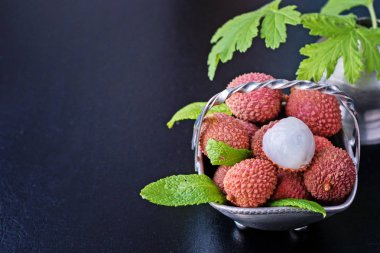 Taze organik liçi meyvesi metal kasede bacakları siyah arka planda, üst manzara