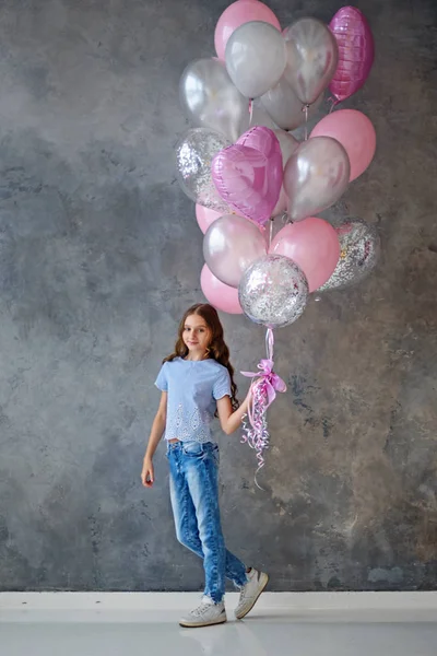 Valentine is a beauty girl with pink, gray balloons laughing, on a gray background. Beautiful happy girl. public holiday. Joyful model posing, having fun, celebrating Valentine\'s day.