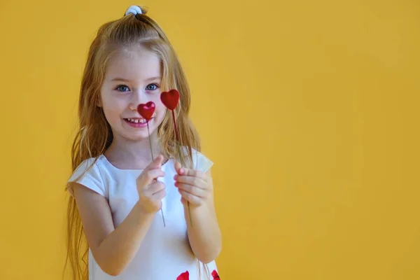 小女孩抱着两个红色的小心脏 情人节的概念 黄色背景 — 图库照片