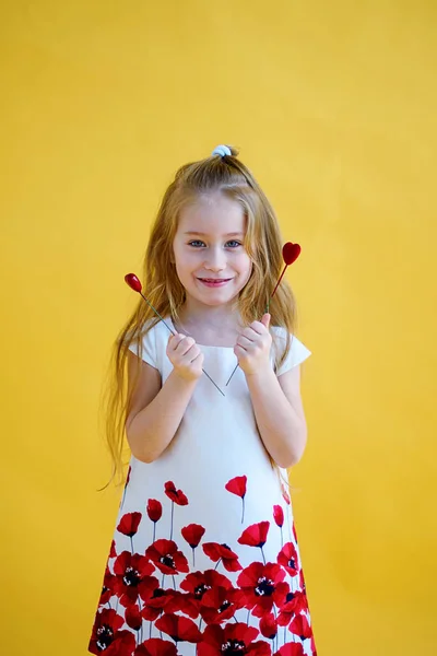 小女孩抱着两个红色的小心脏 情人节的概念 黄色背景 — 图库照片