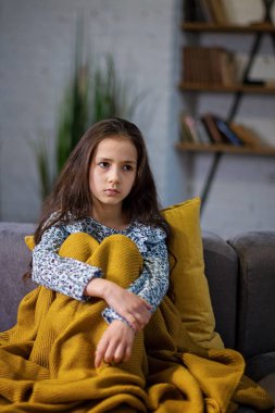 Sarı bir battaniye ile örtülü rahat bir kanepede oturan genç üzgün kız dizlerinin ellerini sıktı.