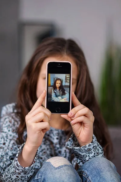 若い十代の少女は 彼女のスマート フォンで Selfie 写真を撮りました 彼の前に彼の写真と彼の手を保持しています — ストック写真