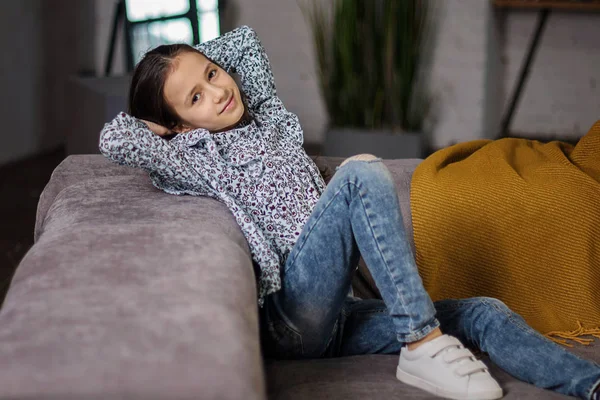 年轻的平静的女孩放松靠在后面 双手放在她的头上舒适的沙发上 疲惫的女孩在客厅的沙发上休息 平静地呼吸 没有压力的周末在家里 — 图库照片
