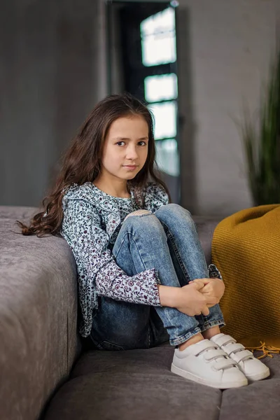 年轻的平静少女长头发 坐在舒适的沙发上 双手紧握她的膝盖 — 图库照片