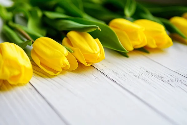 白い木製の背景に黄色のチューリップの花。春を待っています。幸せな母の日、3 月 8 日。フラットの位置、平面図。テキストのための場所. — ストック写真