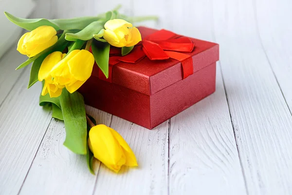 Žluté tulipány květy na bílém pozadí dřevěná s darem. Čekání na jaro. Od hotelu Happy holiday karta. Plochého tvaru, pohled shora. 8. březen. Místo pro text. — Stock fotografie
